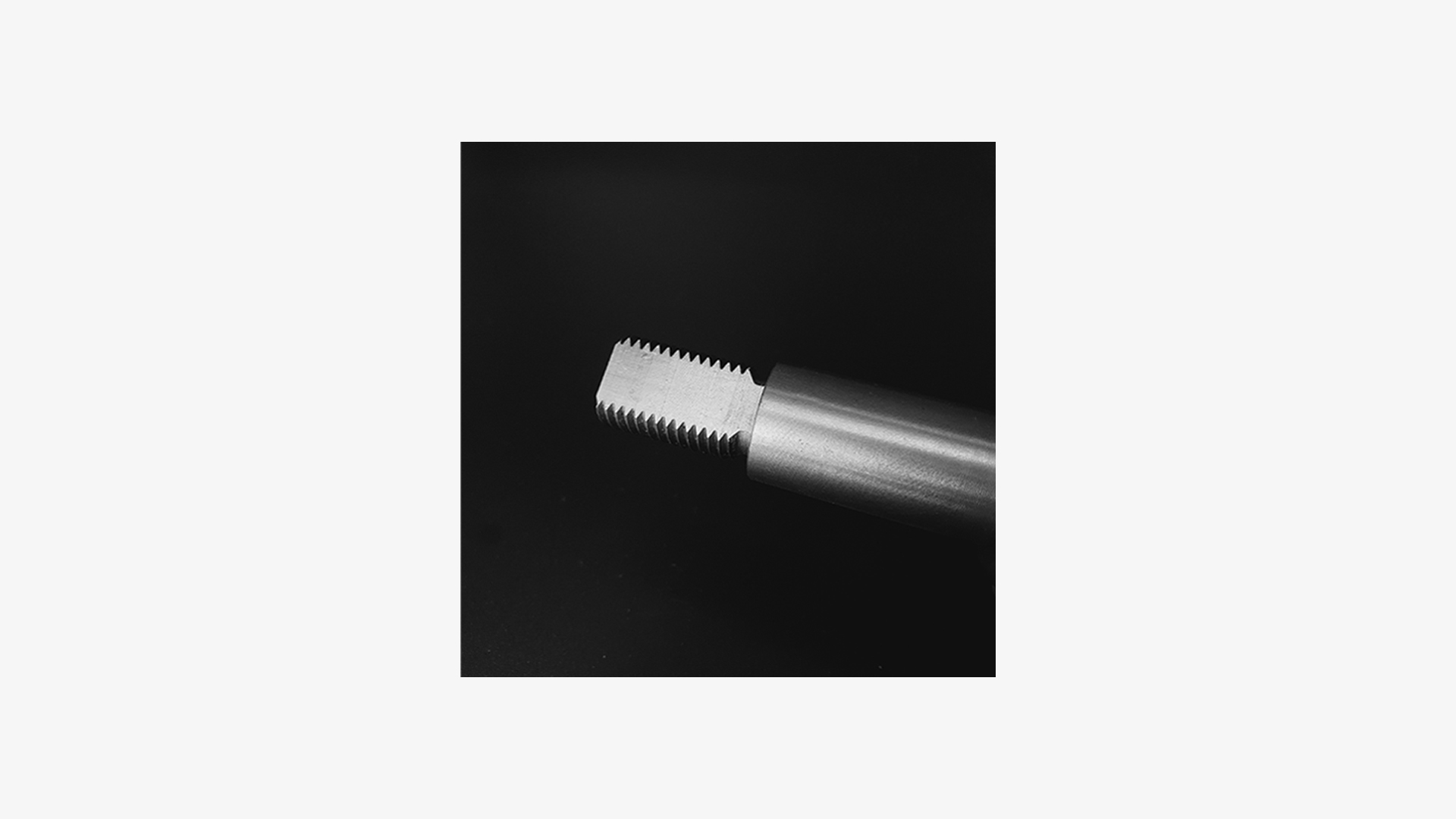 Detail of a metal part with a thread, photographed against a black background with soft side lighting.